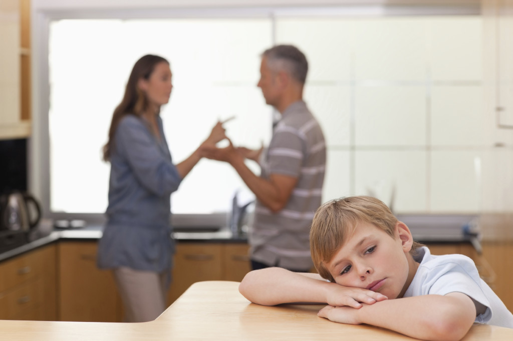 Sad little boy hearing his parents arguing in a kitchen